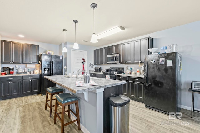 kitchen featuring black appliances, a center island with sink, light hardwood / wood-style flooring, hanging light fixtures, and a breakfast bar area