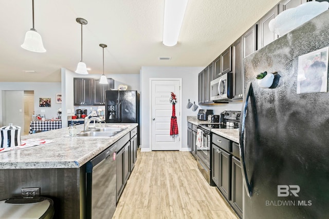 kitchen with stainless steel appliances, sink, decorative light fixtures, a center island with sink, and light hardwood / wood-style floors