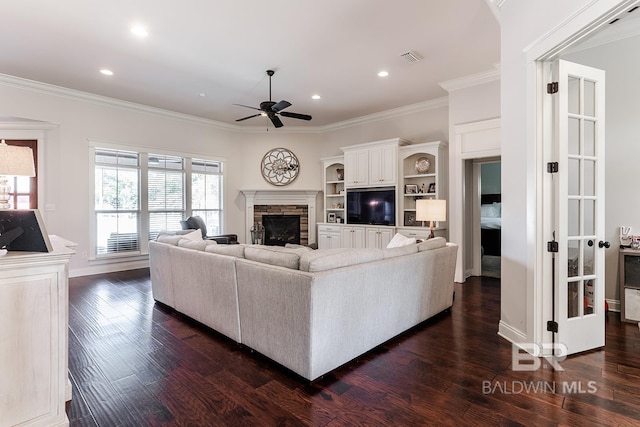 living room with dark hardwood / wood-style floors, a stone fireplace, ceiling fan, and ornamental molding