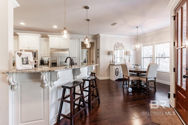 kitchen with hanging light fixtures, stainless steel refrigerator with ice dispenser, light stone countertops, ornamental molding, and white cabinetry