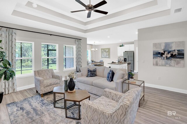 12753 Shoshoney Cir, Fairhope, AL 36532 - living room featuring light wood finished floors, visible vents, baseboards, ceiling fan with notable chandelier, and a raised ceiling