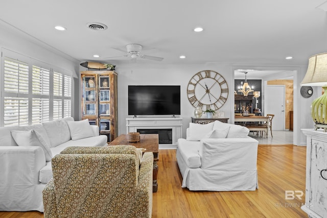 living room with ceiling fan with notable chandelier, light hardwood / wood-style flooring, and ornamental molding