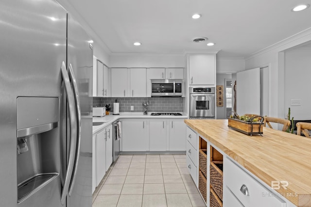 kitchen with tasteful backsplash, light tile patterned floors, ornamental molding, appliances with stainless steel finishes, and white cabinets