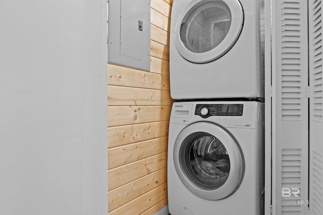 clothes washing area featuring stacked washer / drying machine, electric panel, and wooden walls