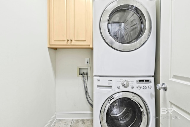 laundry area with stacked washer and dryer, light tile patterned floors, and cabinets