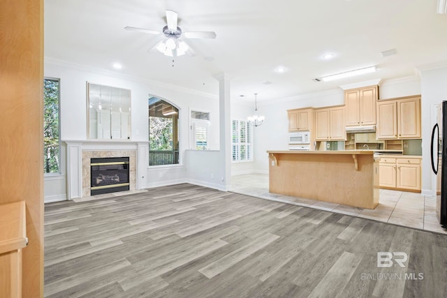 kitchen featuring a kitchen breakfast bar, ceiling fan with notable chandelier, white appliances, light hardwood / wood-style floors, and a kitchen island