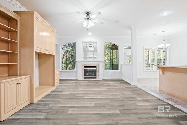 unfurnished living room featuring ceiling fan with notable chandelier, light hardwood / wood-style floors, ornate columns, and crown molding