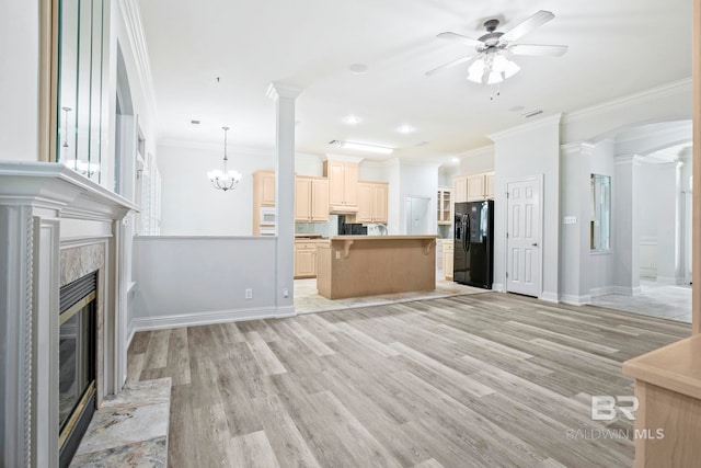 unfurnished living room featuring a high end fireplace, ceiling fan with notable chandelier, ornamental molding, ornate columns, and light hardwood / wood-style floors