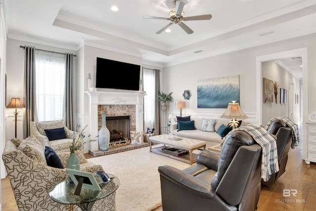 living area featuring a ceiling fan, ornamental molding, wood finished floors, a tray ceiling, and a fireplace