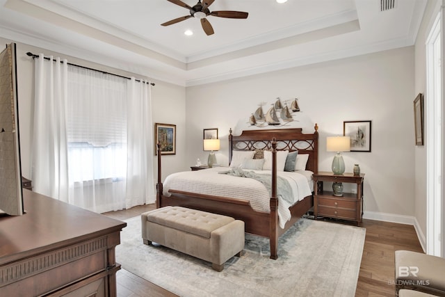 bedroom featuring ornamental molding, a raised ceiling, and wood finished floors