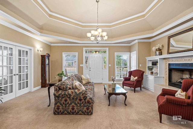 living room with french doors, light carpet, a tray ceiling, a notable chandelier, and a premium fireplace