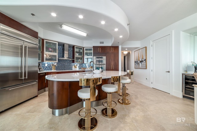 kitchen featuring stainless steel appliances, wall chimney range hood, wine cooler, light countertops, and a kitchen bar