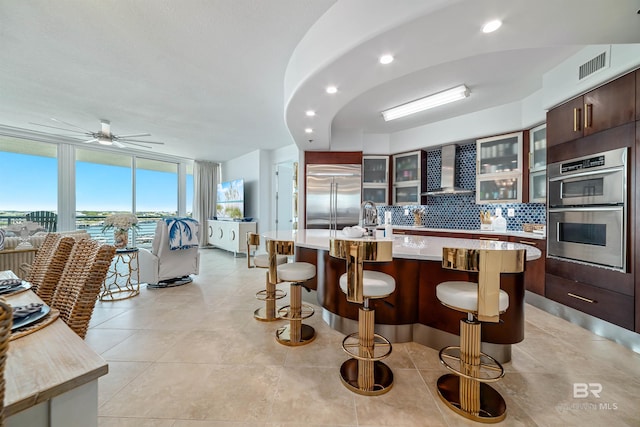 kitchen with stainless steel appliances, wall chimney range hood, a breakfast bar area, visible vents, and light countertops