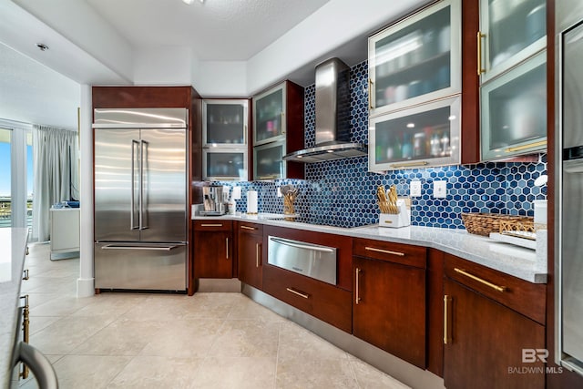 kitchen with backsplash, built in refrigerator, a warming drawer, and wall chimney exhaust hood