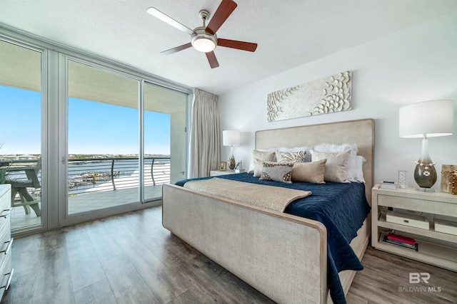 bedroom with access to outside, a water view, a wall of windows, and wood finished floors