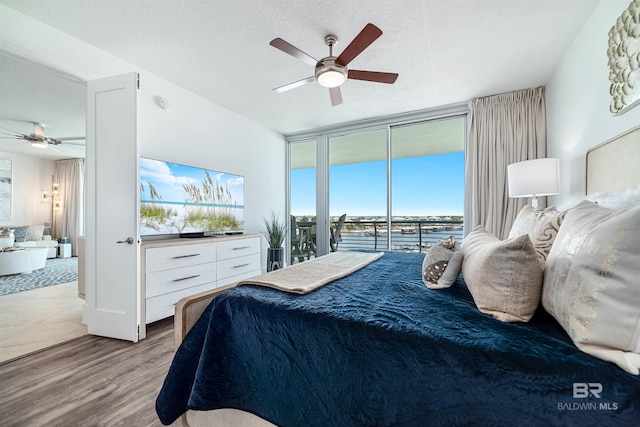 bedroom featuring a wall of windows, access to outside, a ceiling fan, and wood finished floors