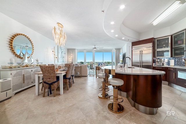 kitchen featuring dark brown cabinets, a sink, stainless steel built in refrigerator, light countertops, and tasteful backsplash