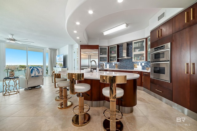 kitchen with visible vents, a kitchen breakfast bar, expansive windows, wall chimney range hood, and appliances with stainless steel finishes