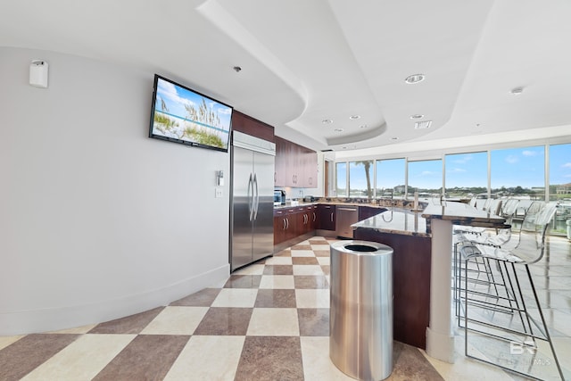 kitchen featuring a peninsula, recessed lighting, a kitchen bar, a tray ceiling, and appliances with stainless steel finishes