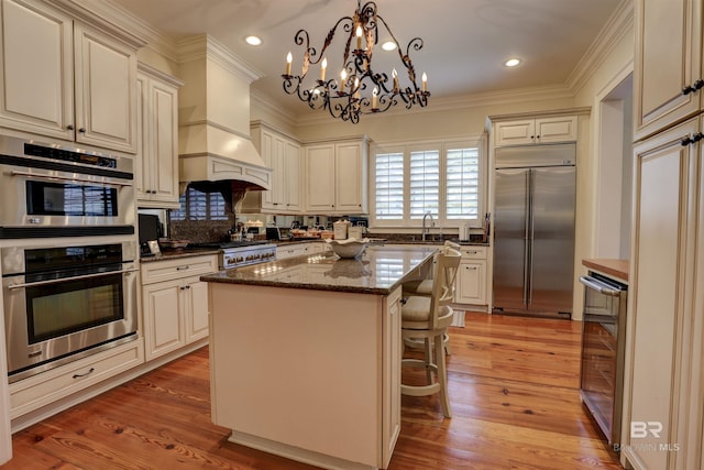 kitchen featuring appliances with stainless steel finishes, light hardwood / wood-style flooring, premium range hood, dark stone counters, and a kitchen island