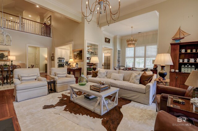 living room with a towering ceiling, hardwood / wood-style flooring, an inviting chandelier, and ornamental molding