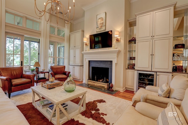 living room featuring light hardwood / wood-style floors, ornamental molding, wine cooler, a notable chandelier, and a towering ceiling