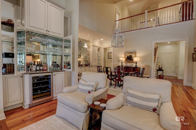 living room featuring light wood-type flooring, wine cooler, a high ceiling, and bar area