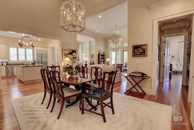 dining area with sink, ornamental molding, hardwood / wood-style floors, and an inviting chandelier