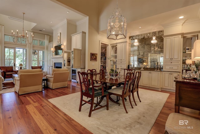 dining area featuring a high ceiling, wood-type flooring, a chandelier, beverage cooler, and crown molding