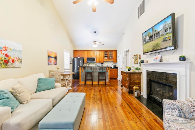 living room with light hardwood / wood-style floors, ceiling fan, and high vaulted ceiling