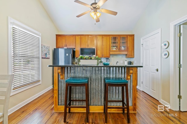 kitchen featuring light hardwood / wood-style flooring, lofted ceiling, stainless steel fridge, and a breakfast bar area