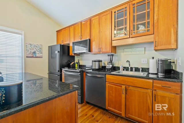 kitchen with stainless steel appliances, dark stone counters, vaulted ceiling, sink, and light wood-type flooring