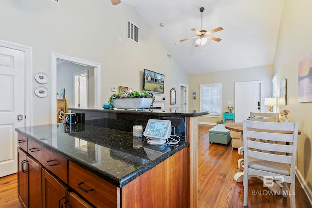 kitchen with high vaulted ceiling, light hardwood / wood-style floors, dark stone counters, and a center island