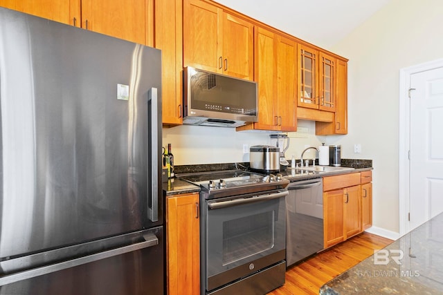 kitchen featuring stainless steel appliances, dark stone counters, light wood-type flooring, sink, and vaulted ceiling