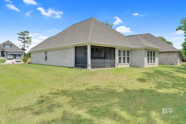 rear view of house featuring brick siding, a lawn, roof with shingles, and a sunroom