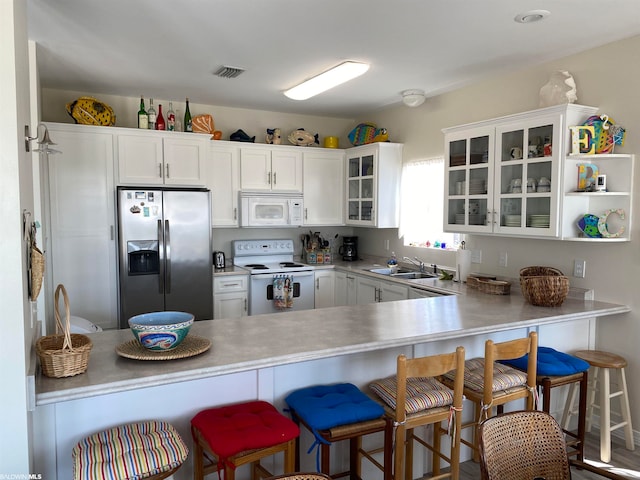 kitchen with kitchen peninsula, white appliances, a kitchen bar, and white cabinetry