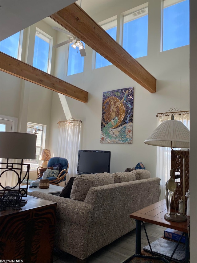 living room with a towering ceiling, ceiling fan, beam ceiling, and wood-type flooring