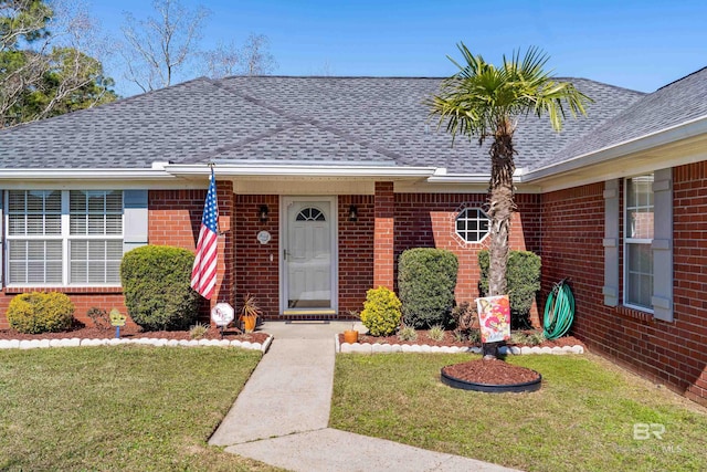 view of front of house with roof with shingles, a front lawn, and brick siding