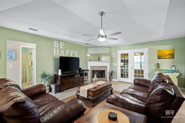 living room featuring french doors, light tile patterned floors, a raised ceiling, visible vents, and a tiled fireplace