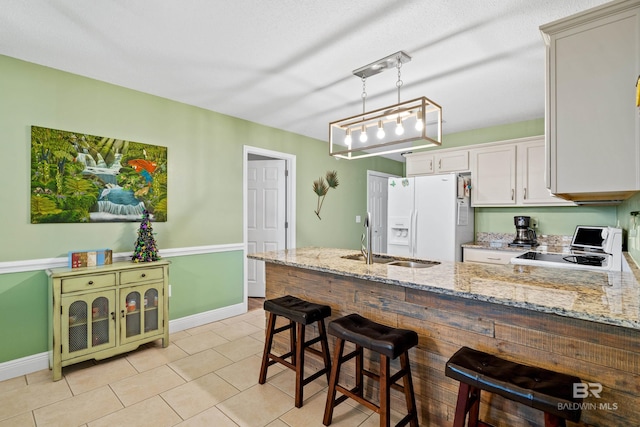 kitchen featuring light stone counters, a peninsula, stove, a sink, and white fridge with ice dispenser