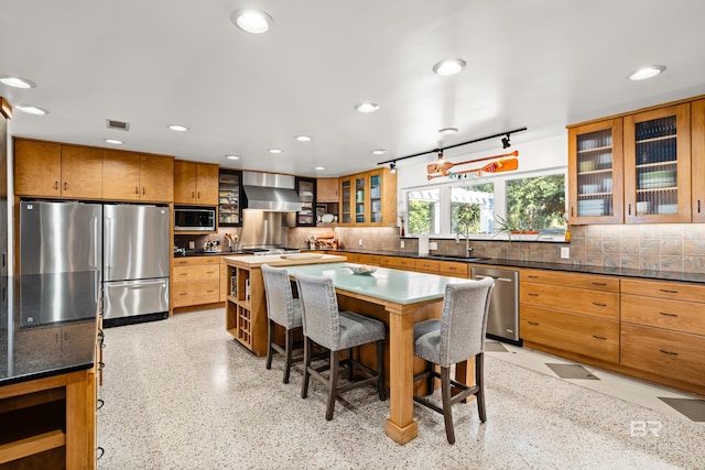 kitchen with a sink, a kitchen breakfast bar, backsplash, stainless steel appliances, and wall chimney exhaust hood