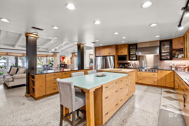 kitchen with visible vents, a kitchen island, glass insert cabinets, appliances with stainless steel finishes, and wall chimney exhaust hood