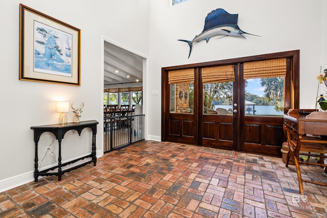 foyer entrance with a high ceiling, baseboards, and brick floor