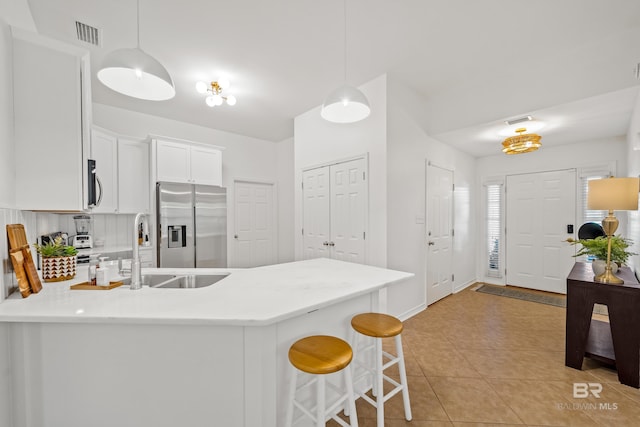 kitchen featuring kitchen peninsula, white cabinets, decorative light fixtures, and appliances with stainless steel finishes