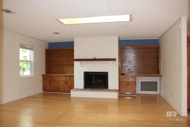 unfurnished living room featuring a fireplace, a textured ceiling, light wood-type flooring, and wooden walls