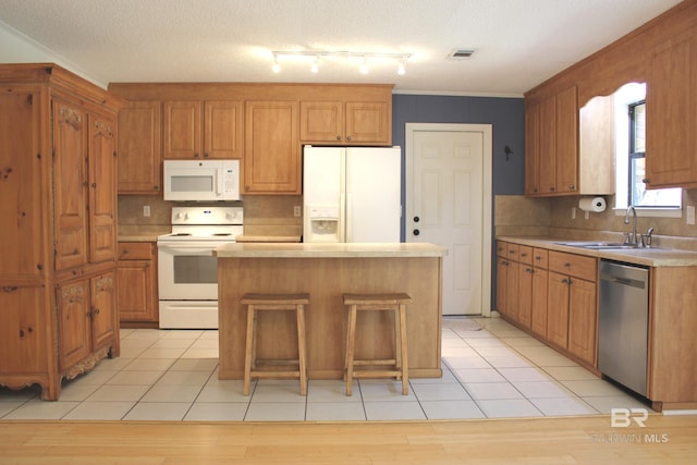 kitchen featuring a textured ceiling, white appliances, sink, a kitchen island, and a breakfast bar area