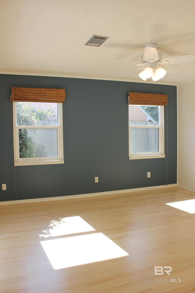 empty room with ceiling fan, plenty of natural light, a textured ceiling, and light hardwood / wood-style flooring