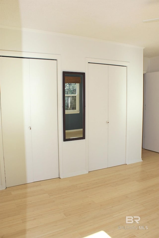 unfurnished bedroom featuring multiple closets and light hardwood / wood-style floors