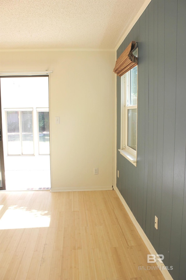 unfurnished room with wood walls, light hardwood / wood-style flooring, and a textured ceiling