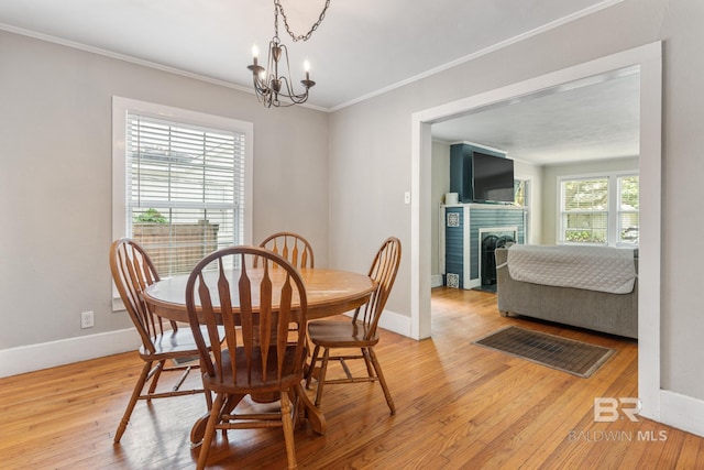 dining space featuring a tiled fireplace, crown molding, light wood-type flooring, and an inviting chandelier